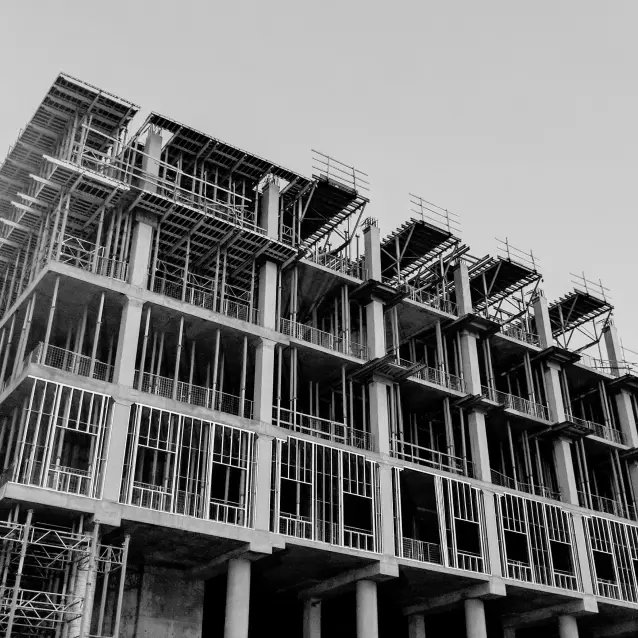 Zwart-witbeeld van een gebouw met meerdere verdiepingen in aanbouw met zichtbare steigers en een onvolledig betonskelet, met de structurele details van Rafaël Mondre.