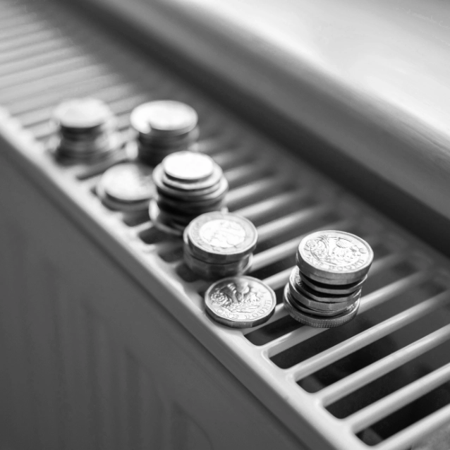 Een zwart-witfoto van Jan Brits met verschillende stapels munten op een geribbeld oppervlak, waarschijnlijk een verwarming, met zacht licht dat vanaf de zijkant naar binnen stroomt.