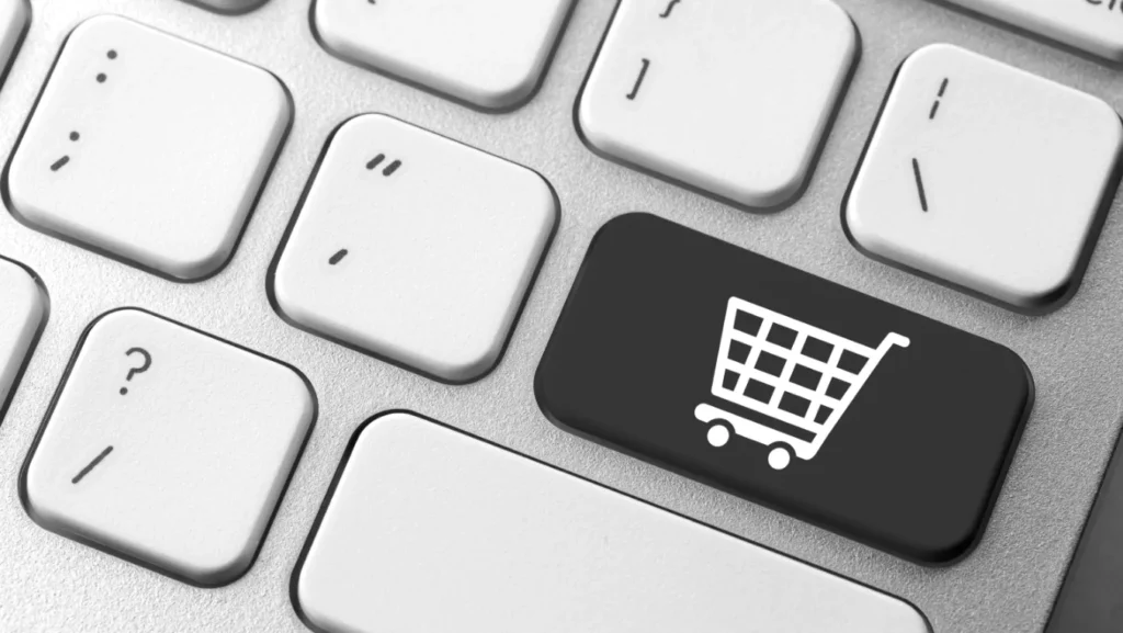 Een close-up van een computertoetsenbord met witte toetsen, met een duidelijke zwarte toets gemarkeerd in het midden. Deze sleutel geeft een wit winkelwagenpictogram weer, dat symbool staat voor online winkelen of webshopfuncties.