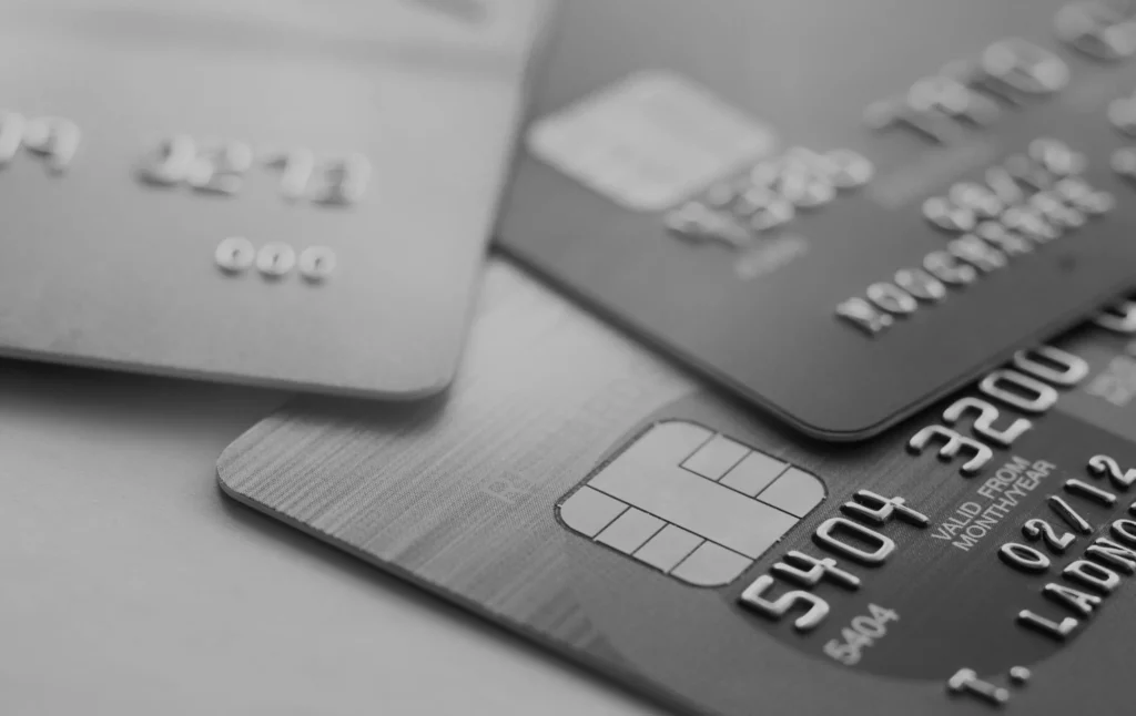 Een grijswaardenafbeelding met drie creditcards erop, met de nadruk op nummers, namen en vervaldatums in reliëf, met een prominente beveiligingschip zichtbaar op de dichtstbijzijnde kaart.
