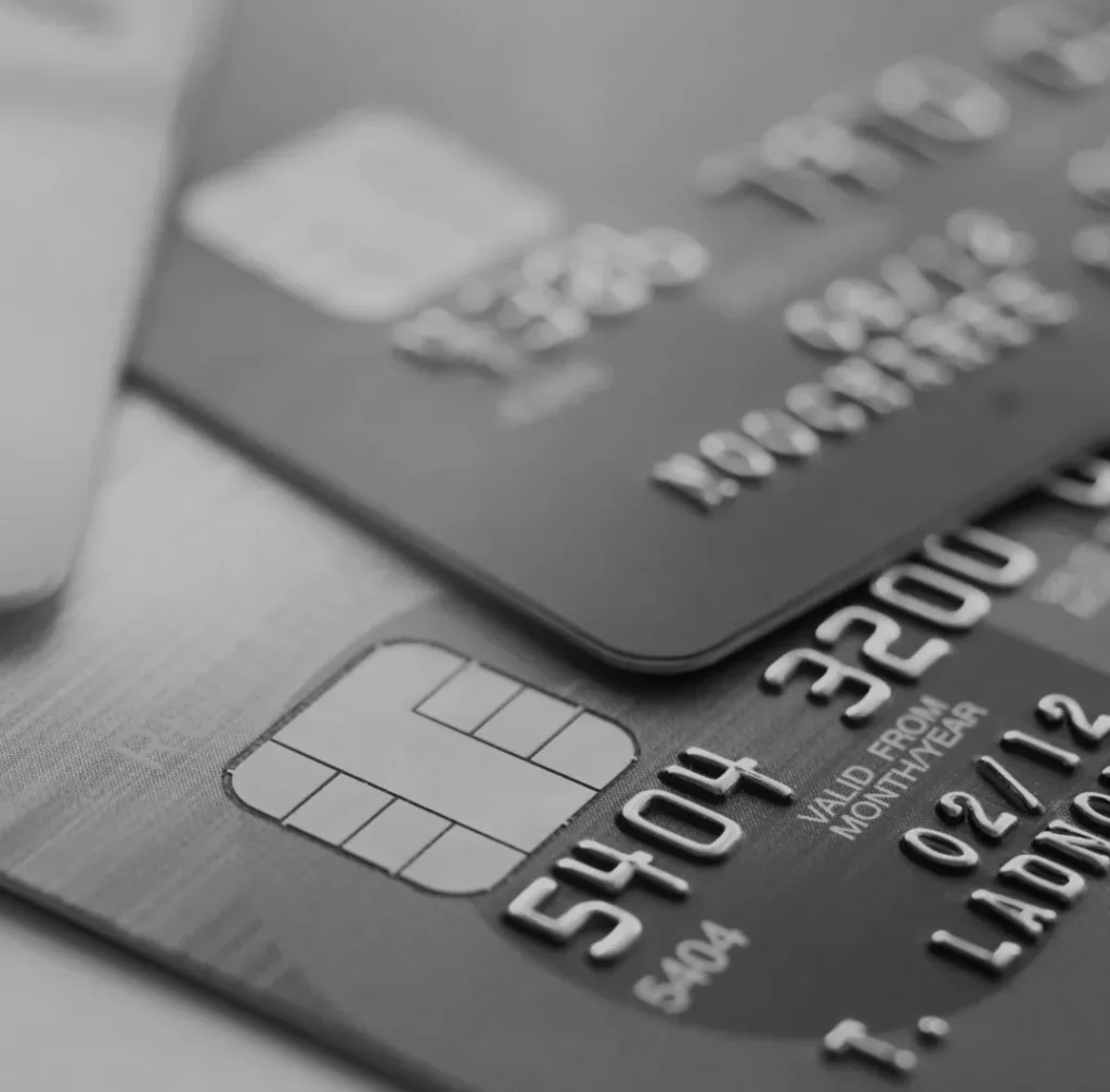 Zwart-wit close-up van meerdere creditcards, met de nadruk op de reliëfnummers, chip en vervaldatum, waarbij de textuur en details van het oppervlak van de kaarten worden weergegeven.