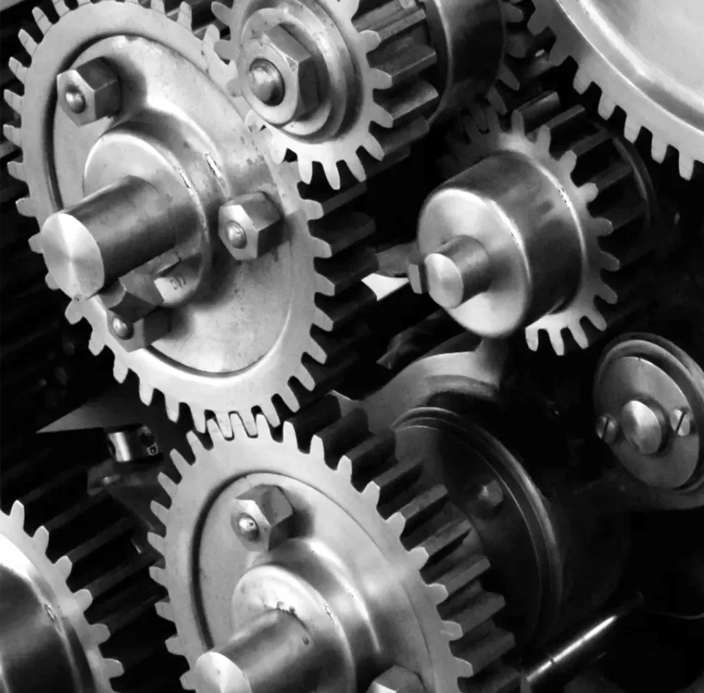 Een zwart-witafbeelding met een close-up van onderling verbonden metalen tandwielen en tandwielen, elk met een zichtbare as en veilig gemonteerd, wat de complexiteit van mechanische systemen aantoont.