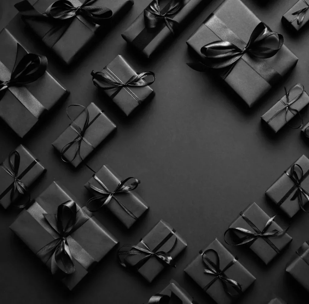 Een monochrome afbeelding met verschillende zwarte geschenkdozen van verschillende afmetingen, allemaal vastgebonden met elegante zwarte linten, netjes gerangschikt op een donkere achtergrond. het arrangement vertoont een minimalistische en luxueuze esthetiek.
