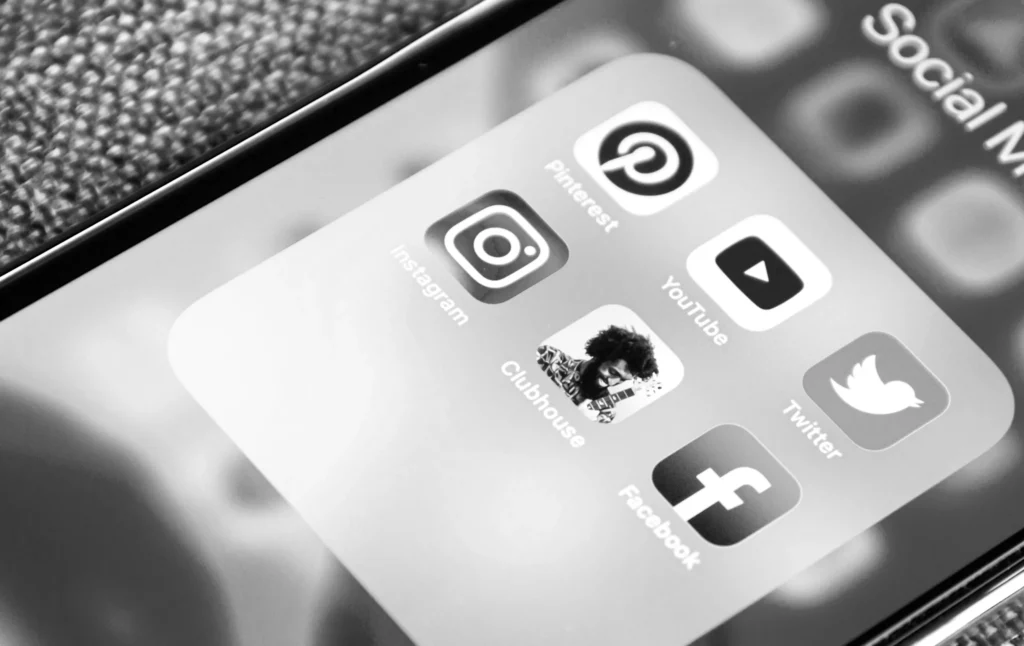 Een monochrome close-upfoto van een smartphonescherm met verschillende app-pictogrammen voor sociale media, zoals Instagram, YouTube, Twitter, Facebook, Pinterest en clubhuis, in een map met het label 'sociale media'.